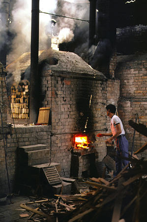 Worker throwing wood into a kiln at the terra cotta factory in Xi'an. China.