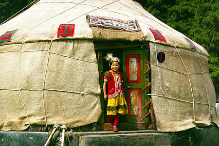 Child in colorful clothing in doorway of a yurt in Uighur village near Urumqi. China.