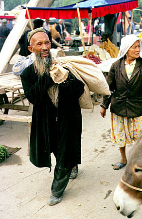 Man carries bags of goods through the Sunday market in Kashgar. China.