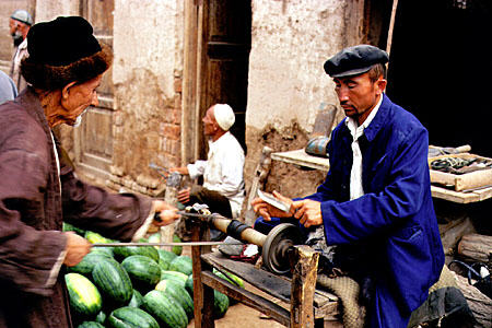 Sharpening knives by using a leather strap to turn lathe at Sunday market, Kashgar. China.