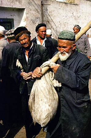 Elderly man carries his goods through the Sunday market in Kashgar. China.