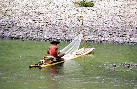 Fisherman repairs nets while sitting on his bamboo raft on the Li River. China.