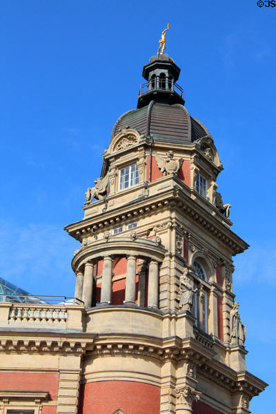 Upper level of an Old Post Office tower covered with decorative architectural elements & topped by golden Mercury. Hamburg, Germany.