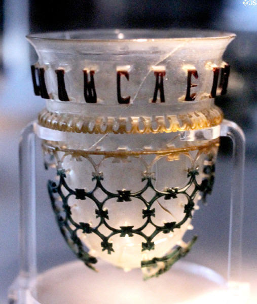 Ancient Roman Vasa Diatreta or cage cup (4C) with Greek inscription on rim & outer tracery in colored relief at Roman Germanic Museum. Köln, Germany.