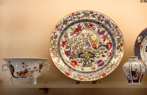 Meissen porcelain plate (c1740s) painted with colored versions of Zwiebelmuster (blue onion) pattern plus other vessels with East Asian designs at Meissen porcelain museum at Lustheim Palace. Munich, Germany.