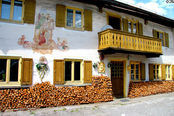 Traditional Bavarian style building with firewood stacked against length of building & religious themed fresco on front facade. Oberammergau, Germany.