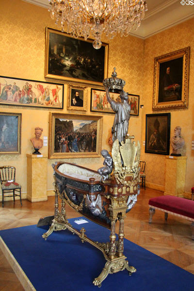 Cradle of the Crown Prince, Eugène-Louis (1856) with a grand figure modeled by Pierre-Charles Simart holding a crown above the baby at Carnavalet Museum. Paris, France.