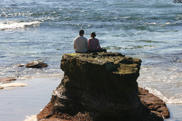 Couple sit on rocks at ocean in La Jolla Cove. La Jolla, CA.