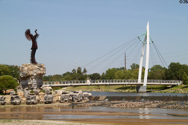 Pedestrian suspension bridge structure (2007) over Arkansas Rivers beyond Keeper of the Plains sculpture. Wichita, KS.