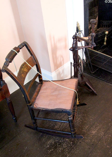 Hitchcock rocking chair with caned seat as stenciled by Rose Standish Nichols & flax wheel in rear bedroom at Nichols House Museum. Boston, MA.