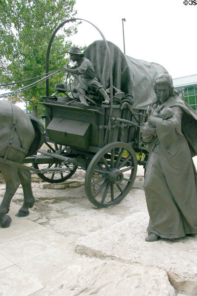 Sculpted woman with child walks beside covered wagon of Wagon Trail Monument. Omaha, NE.