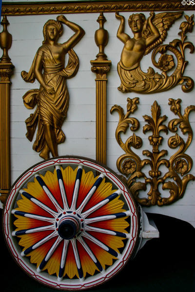 Golden circus wagon detail of mythical figures over bright wagon wheel at Circus World Museum. Baraboo, WI.