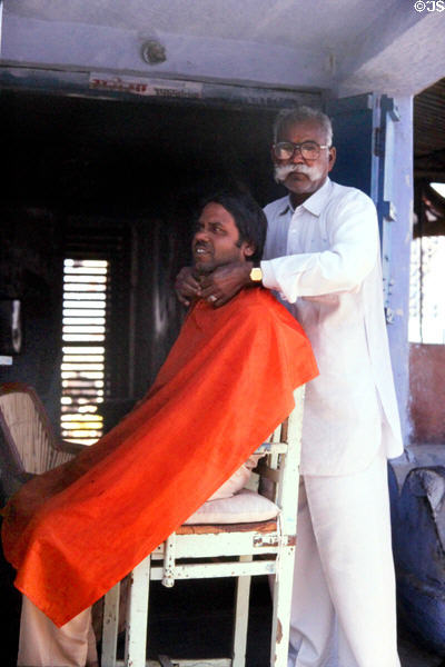 Barber giving a haircut to a man in Roopangarth. India.