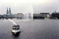 Fountain in Binnenalster Lake with Germany's oldest steamboat, St Georg, providing a tourist cruise. Hamburg, Germany