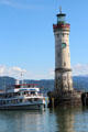 Sightseeing boat passing lighthouse at harbor entrance. Lindau im Bodensee, Germany.