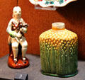 Stained creamware bagpipe player figure & earthenware tea jar in pineapple form with green & yellow glazes both from Staffordshire at Potteries Museum & Art Gallery. Hanley, Stoke-on-Trent, England.