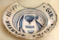 Tin-glazed earthenware shaving bowl painted with barber tools & message 'Sir youre quarter is up' since shaving bills were paid 4 times per year from Lambeth, London at British Museum. London, United Kingdom.