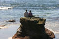 Couple sit on rocks at ocean in La Jolla Cove. La Jolla, CA.