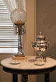 Glass kerosene lamp & silver tea urn in Chillman Parlor at Bayou Bend. Houston, TX.