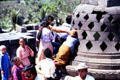 Visitors try to touch Buddha covered by stone lacework stupa at Borobudur. Indonesia