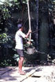 Man lowers bucket on pole into well. Jogyakarta, Indonesia.