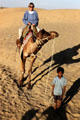 Boy leads a tourist riding a camel across Sam Sand Dunes. India.