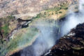 Mist rises from Victoria Falls with bridge in background. Zimbabwe.