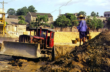 Men carrying dirt on shoulder polls alongside bulldozer at construction site in Kweilin. China.