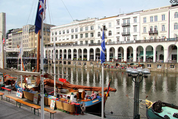 Heritage canal boat docked on Kleiner Alster canal with Venetian-style arcade on opposite shore. Hamburg, Germany.