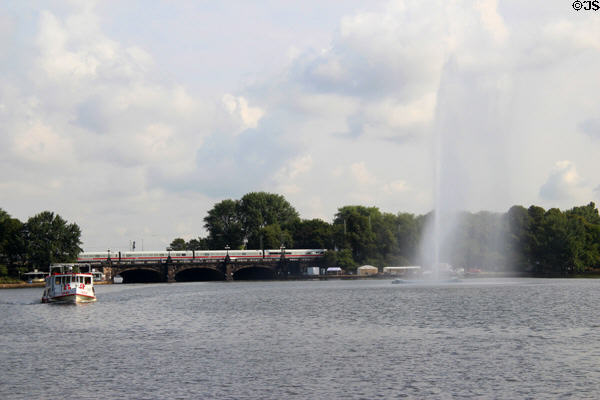 Water spout fountain with passenger train crossing bridge between inner & outer Alster. Hamburg, Germany.