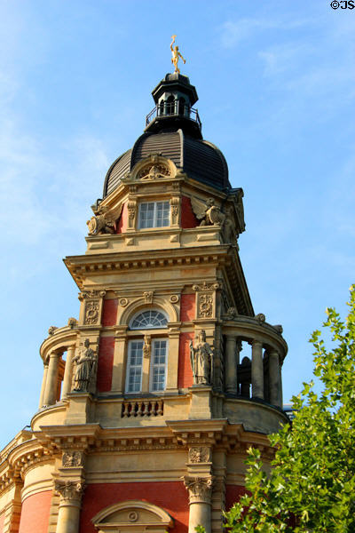 Upper level of an Old Post Office tower covered with decorative architectural elements & topped by golden Mercury. Hamburg, Germany.