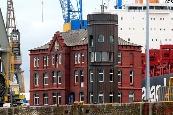 Thyssenkrupp Marine Systems building with stepped roof & Hamburg coat-of-arms against cranes & container ship. Hamburg, Germany.