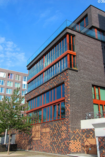Modern building with red trim around windows where decorative brick of flood barrier has been extended upward on Dalmannkai in HafenCity. Hamburg, Germany.