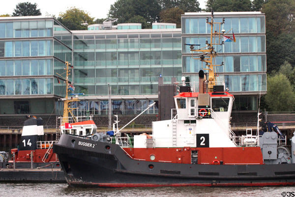 Tugboat moored on Elbe River in front of modern glass building in Altona borough. Hamburg, Germany.
