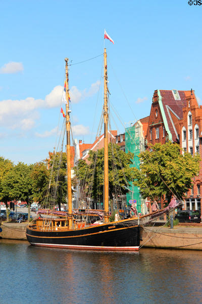 Sailing ship docked on Trave River before heritage buildings. Lübeck, Germany.