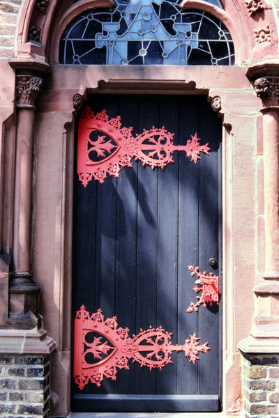 Church door with ornate pink hinges & stained glass fan window. Zons, Germany.