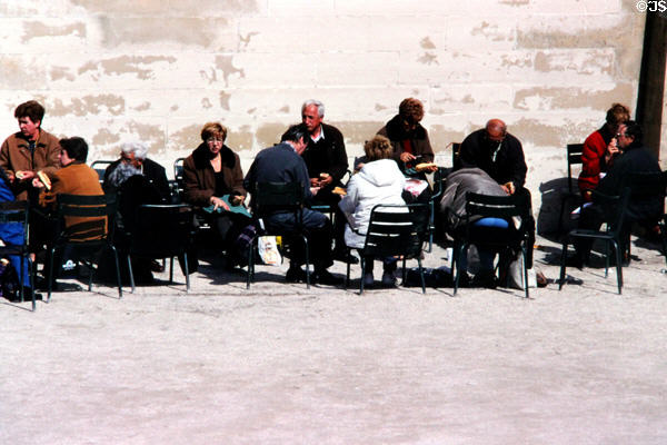 Parisians sunning themselves against wall in Tuileries Garden. Paris, France.