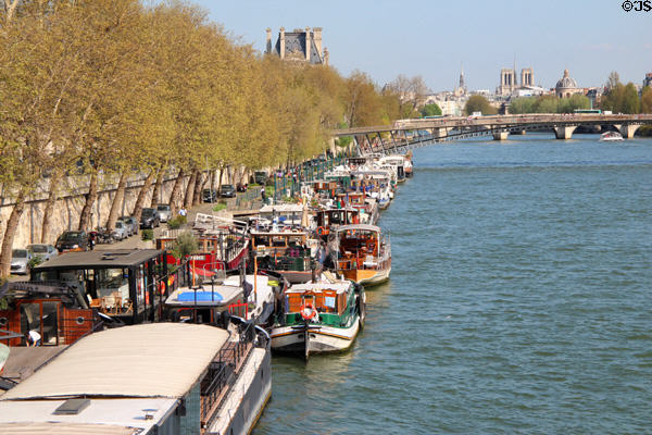 Triple parking houseboats near Passerelle Léopold-Sédar-Senghor footbridge over Seine. France.