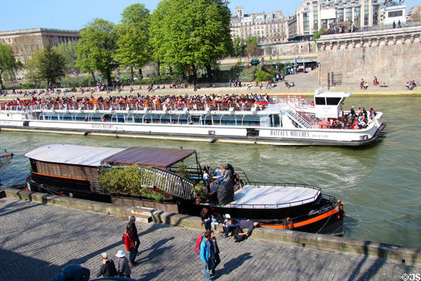 Tourist boat passes walkers on Seine. Paris, France.