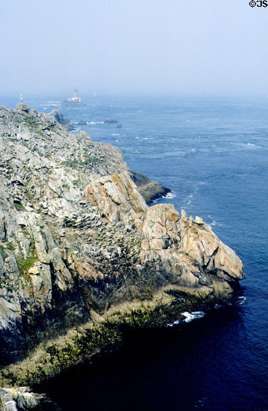 View of rocks & dangerous waters with lighthouses in distance. Pointe du Raz, France.
