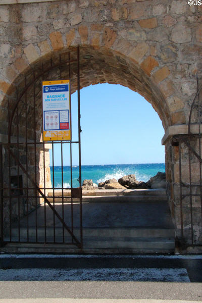 View through harbor wall of waves crashing on rocks. Antibes, France.