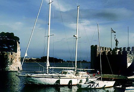 Sail boat in harbor of Nafpaktos is protected by a Venetian wall seen in the distance. Greece.