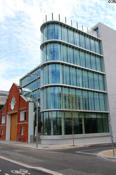 Glass facade of Campshire Hall wraps around preserved facade of old quayside warehouse on Sir John Rogerson's Quay. Dublin, Ireland.
