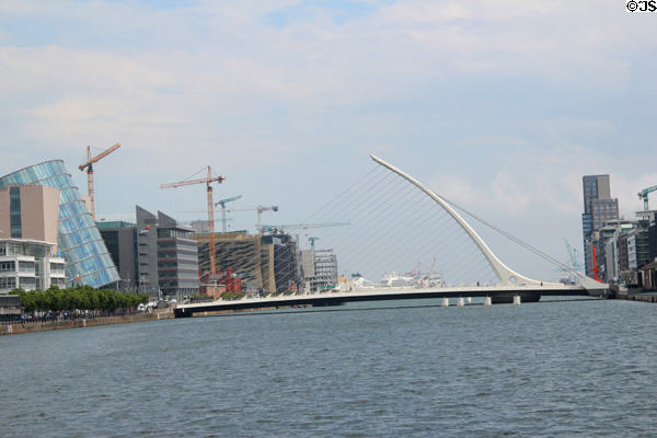 Samuel Beckett Bridge over River Liffey with leaning glass cylinder or Dublin Convention Center on left & Dublin's tallest complex Capital Dock in distance on right. Dublin, Ireland.