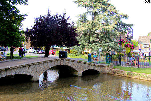 Arched footbridge crossing River Windrush in town center. Bourton-on-the-Water, England.