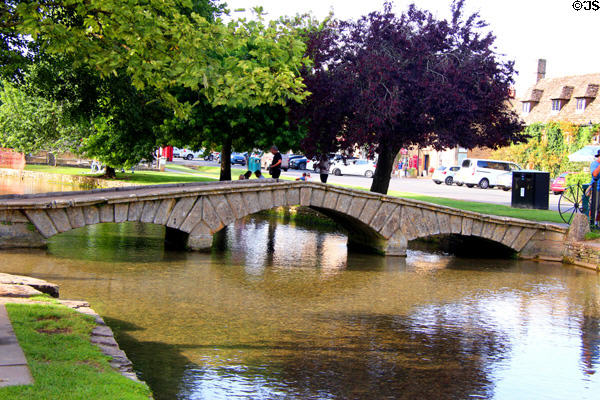 Arched footbridge crossing River Windrush in town center. Bourton-on-the-Water, England.