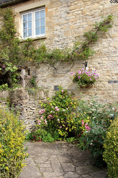 Old brick wall with climbing plant & garden along stone walkway. Bourton-on-the-Water, England.