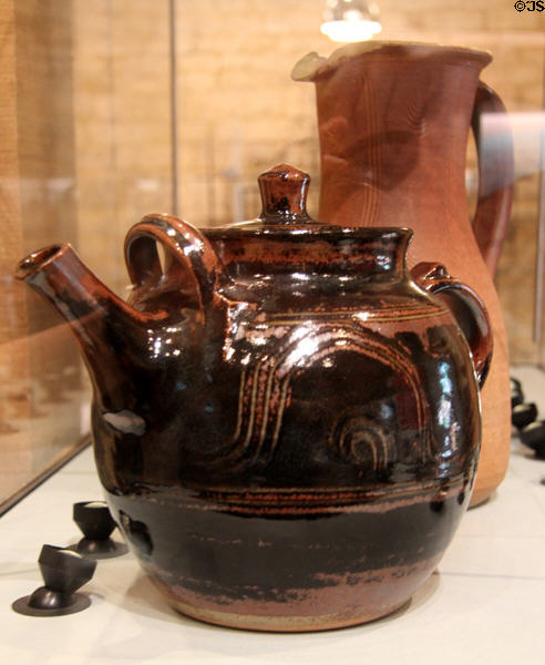 Teapot (c1990's) with Winchcombe iron glaze & wavy line decoration by Ray Finch & stoneware jug (c1980's) also by Ray Finch in background at Court Barn Museum. Chipping Campden, England.