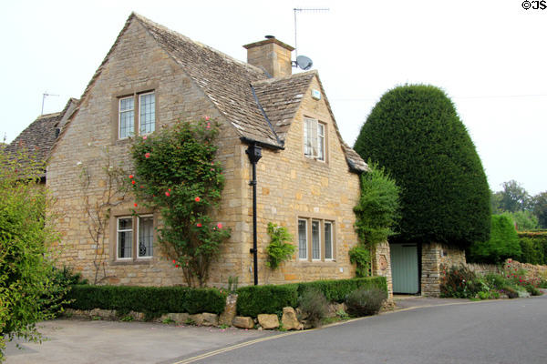 Cotswold stone home with slate roof & climbing red roses on side. Lower Slaughter, England.