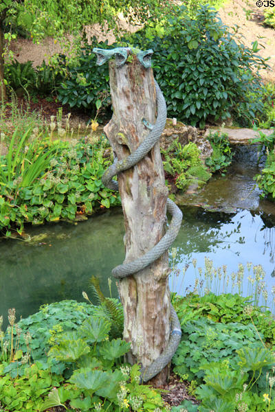 Snake statue coiled on tree trunk by stream at Sezincote. Moreton-in-Marsh, England.